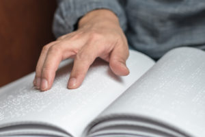 Interested in learning Braille? Image shows hand on a braille book