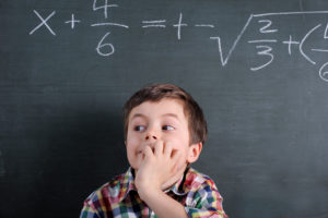 The image indicates maths anxiety by showing a child standing infront of a maths problem looking worried