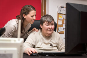 A mentally disabled lady in front of a computer accessing easy read with a carer by her side